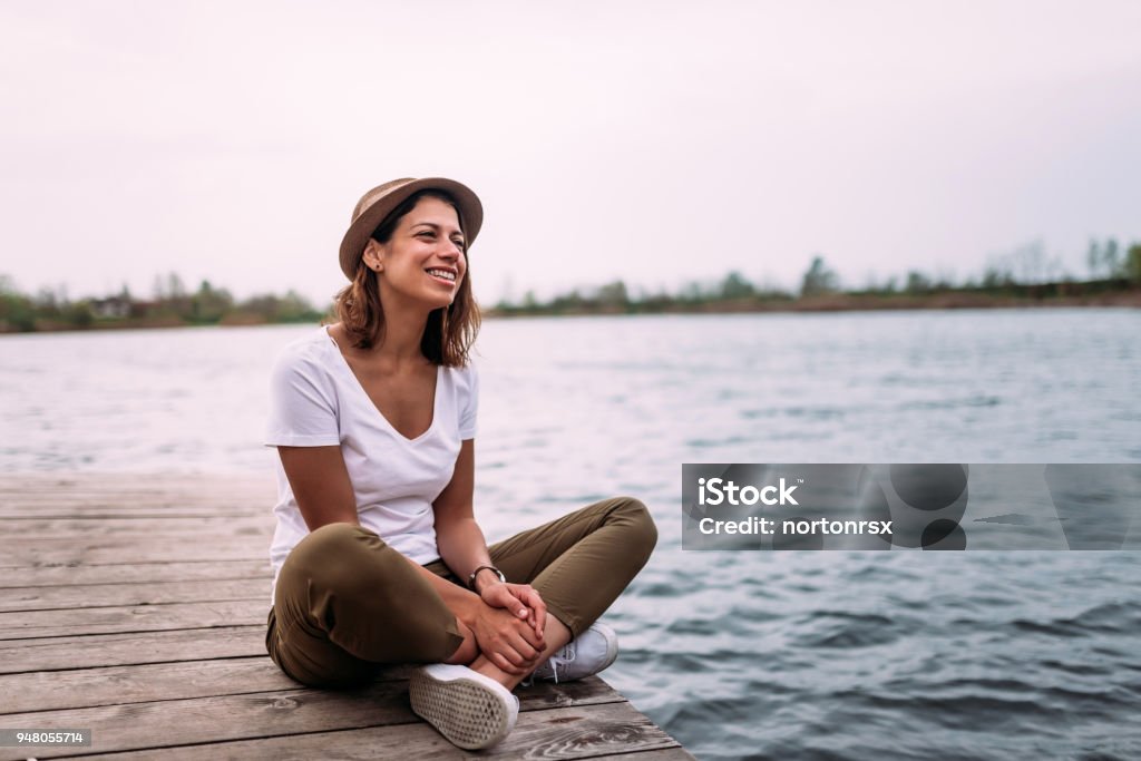 Young woman relaxes on the edge of a wooden jetty. Women Stock Photo