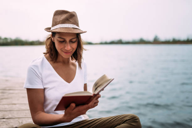 istock Young female student reading book while sitting near water. 948055804