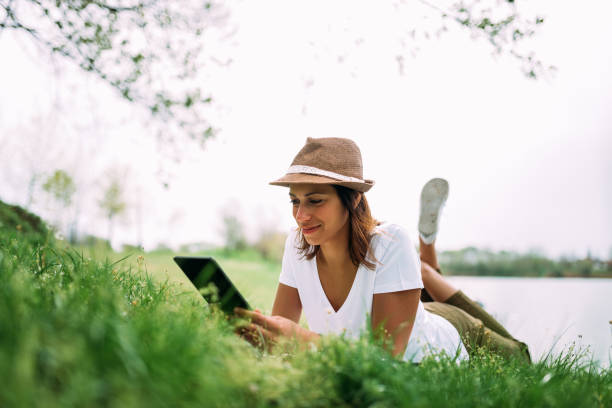 istock Young woman using tablet outdoor laying on grass, smiling.