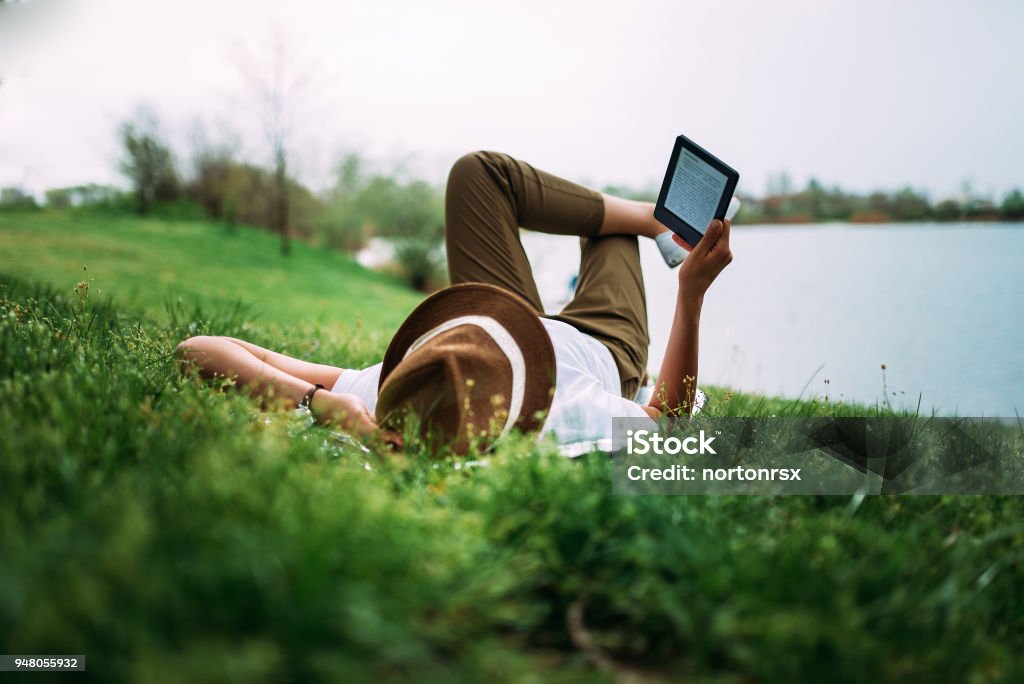 Enjoying day outdoors. Reading a book next to lake while laying on the grass. Reading Stock Photo