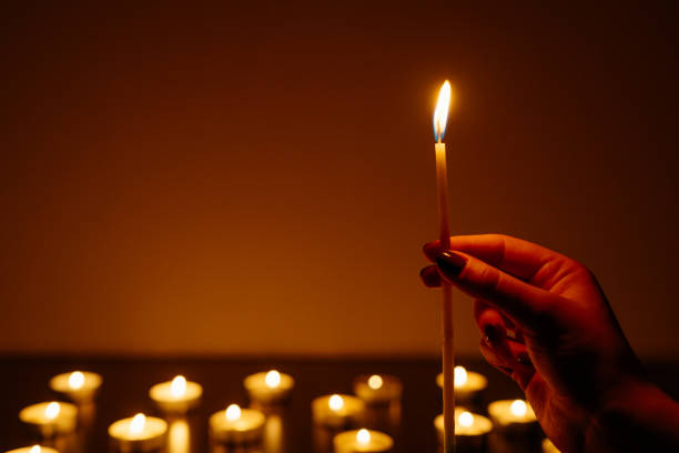 istock Woman's hands holding a burning candle. Abstract candles background. Many candle flames glowing on dark background. Close-up. Free space. 948068880