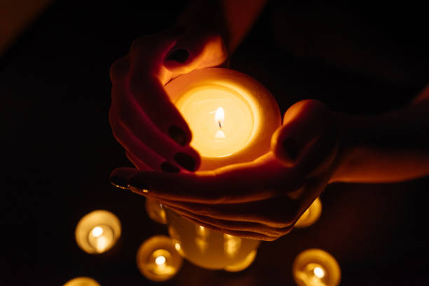 istock Woman's hands holding a burning candle. Abstract candles background. Many candle flames glowing on dark background. Close-up. 948069934