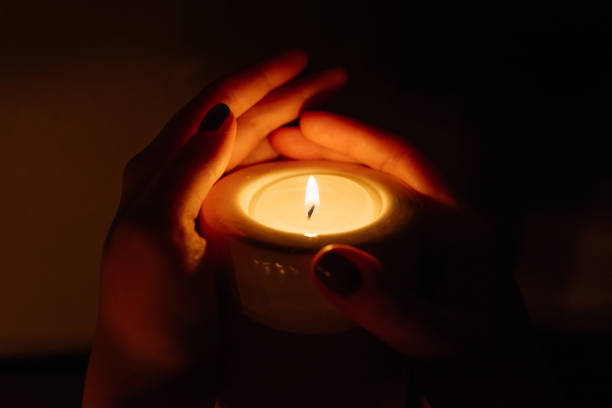 istock Woman's hands holding a burning candle on dark background. Close-up. 948070142