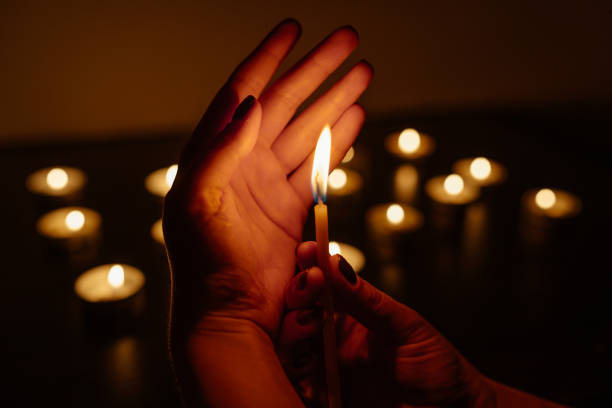 istock Woman's hands holding a burning candle. Abstract candles background. Many candle flames glowing on dark background. Close-up. 948070812
