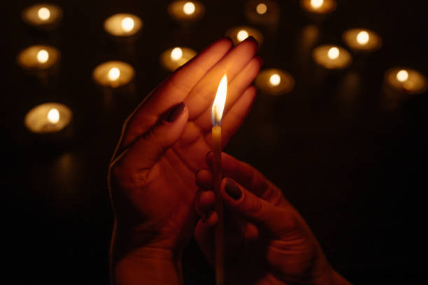 istock Woman's hands holding a burning candle. Abstract candles background. Many candle flames glowing on dark background. Close-up. 948072900