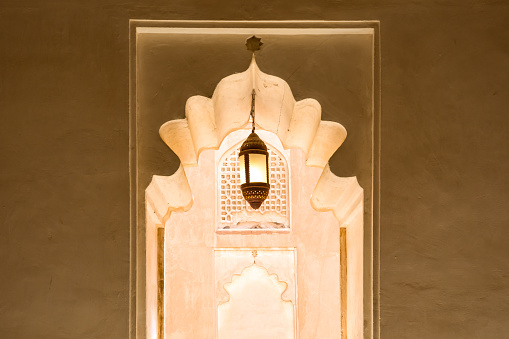 A lighted arabic style lamp hanging over a decorated hallway on a warm afternoon. Nizwa, Oman.