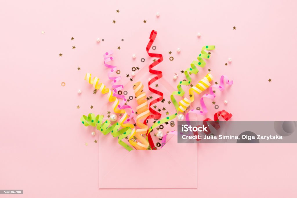 Party confetti & sequins explosion from envelope on pink Confetti & sequins explosion. Opened envelope with festive streamers on pink background. Party Invitation concept. Flat lay, minimal style. Confetti Stock Photo