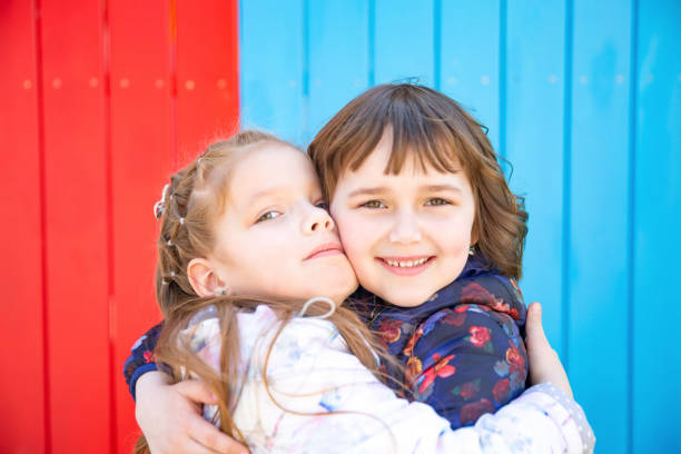 Happy little girlfriends embrace outdoor. Colourful background