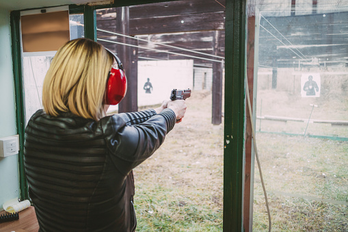 Woman firing with pistol on target at the shooting range. Rear view.