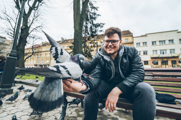 istock young man feed doves in city park. 948163652