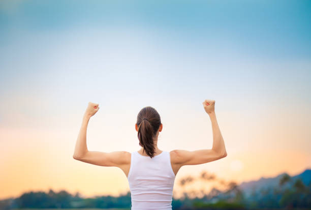 mujer fuerte flexionando sus músculos contra la puesta de sol. - human muscle women bicep girl power fotografías e imágenes de stock