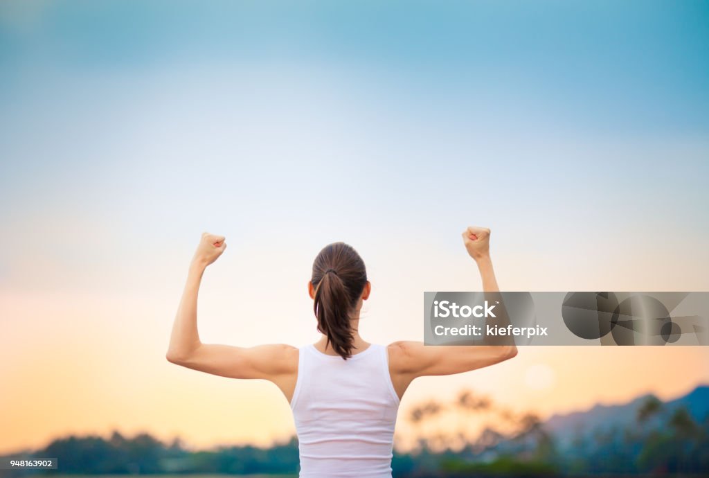 Mulher forte flexionando seus músculos contra o pôr do sol. - Foto de stock de Girl Power-provérbio em Inglês royalty-free