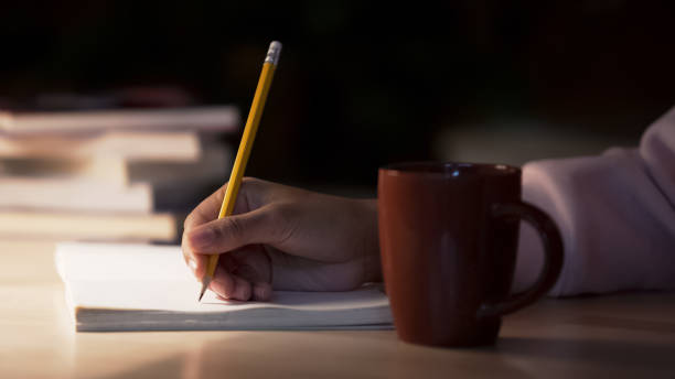 istock Biracial student writing essay in library, tea cup standing on desk, closeup 948171604