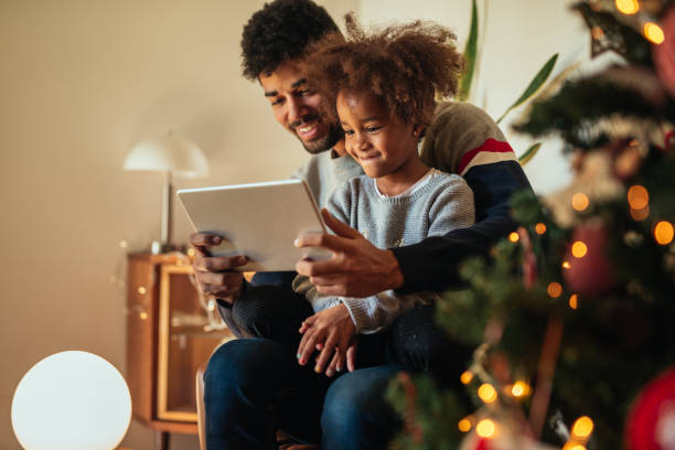 Christmas relaxment at home Cute african american girl using tablet with dad at home. holiday shopping stock pictures, royalty-free photos & images