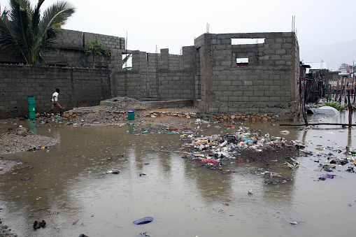 Cap Haitien, Haiti - March 16, 2018: A boy jumps over a puddle of essentially raw sewage in the Aviasyon neighborhood, which is subject to frequent flooding and home to SOIL clients in its EkoLakay Ecosan home composting toilet service.  SOIL provides and services the toilets, which provide the basic elements, human waste and shredded vegetable matter, of compost that will, once completed and tested for pathogens, be used to grow fruits and vegetables.