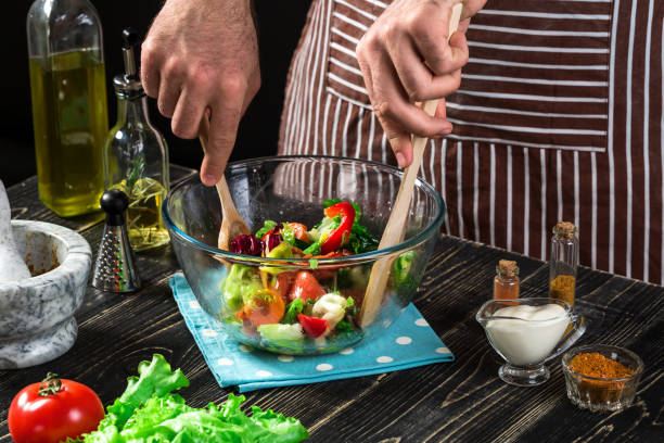 Man preparing salad with fresh vegetables on a wooden table. Cooking tasty and healthy food