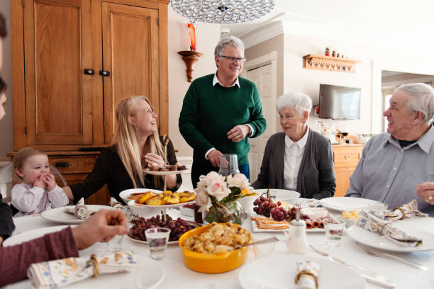 Big family dinner including mult-generation family like senior and millennial family. Big family dinner including senior couple, millennial family and adult around the table. This photo can be use also for mother's day, father's day, birthday, valentine's day, Easter Time and Christmas. They are really people.The table is well done with flowers and foods. The little girl of 2 years old is eating strawberries. Photo was taken in Quebec Canada. big family table stock pictures, royalty-free photos & images
