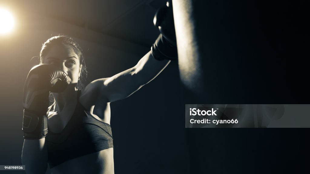 Boxer woman training at the gym Young woman doing boxing training at the gym, she is wearing boxing gloves and hitting the punching bag Boxing - Sport Stock Photo