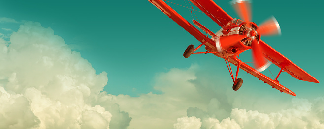 Red biplane flying in the cloudy sky. Retro style