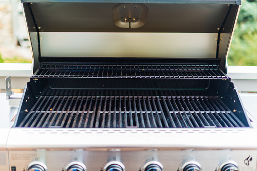Six burner outdoor gas grill with open lid on backyard.