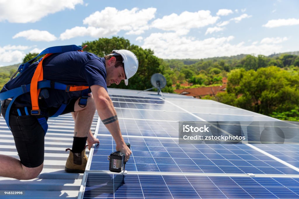 Solar panel technician with drill installing solar panels Solar panel technician with drill installing solar panels on roof on a sunny day Solar Panel Stock Photo