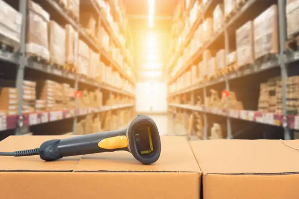 Barcode scanner in front of modern warehouse and scanning code on cardboard box