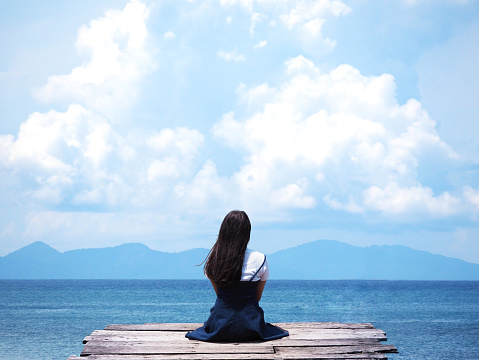 asian girl sitting on wooden bridge over blue sea