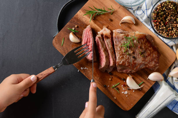 istock little hand cutting beef steak on top view 948411558