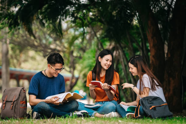 Young asian student. A group of young or teen Asian student in university smiling and reading the book and look at the tablet or laptop computer in summer holiday. teenagers only stock pictures, royalty-free photos & images