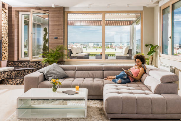 istock Young black woman reading a book while relaxing on sofa at home. 948426174