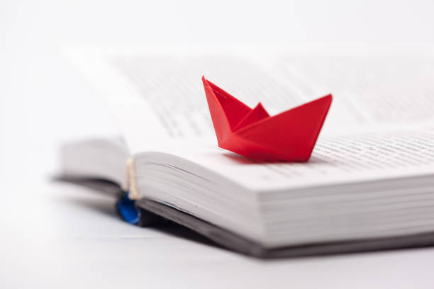 istock Origami paper boat on a book 948430420
