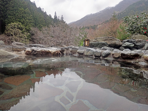 Traditional japanese onsen, stone outdoor bath, hills and forest in background, sunny day, nature of Gunma, Japan