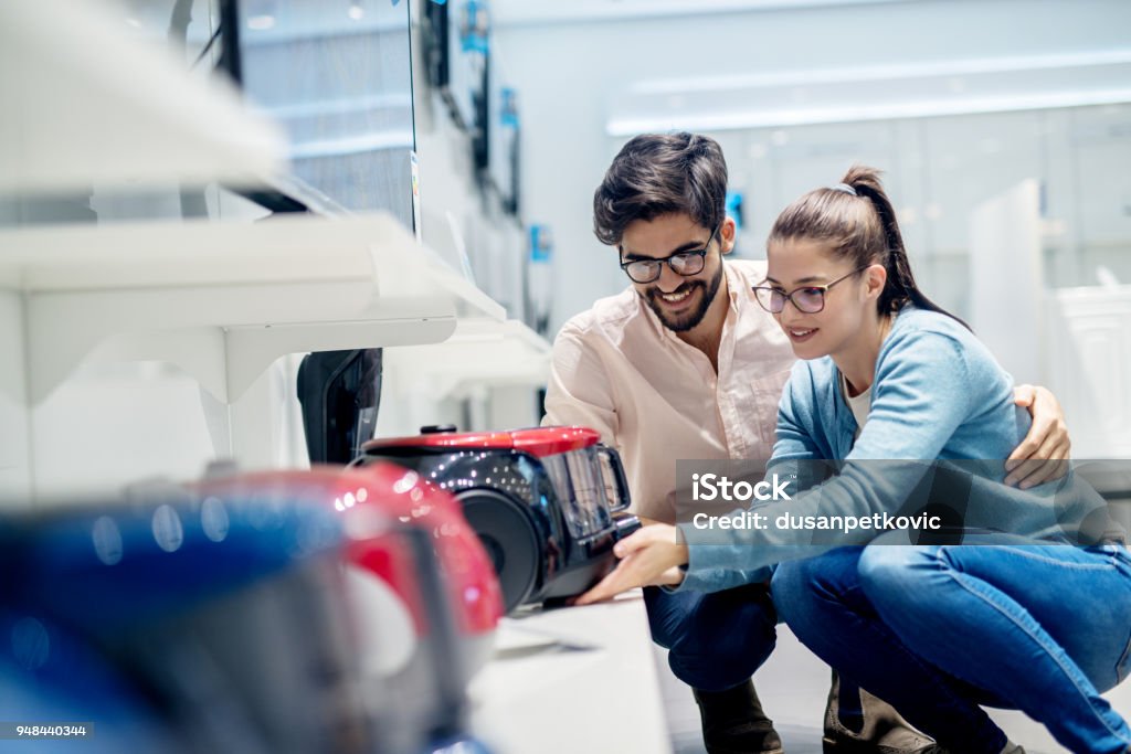 Young lovely husband and wife deciding which vacuum cleaner to buy in the electronic store. Shopping Stock Photo