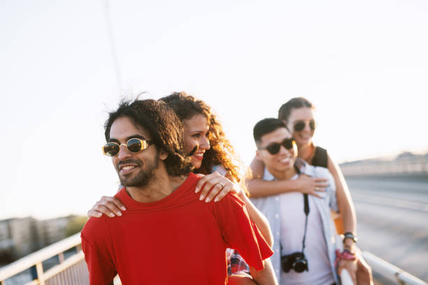 istock Group picture of two young man holding girlfriends on their backs while walking on a beautiful day. 948443532