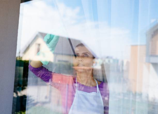 istock Young beautiful woman in white apron cleaning windows. 948444068