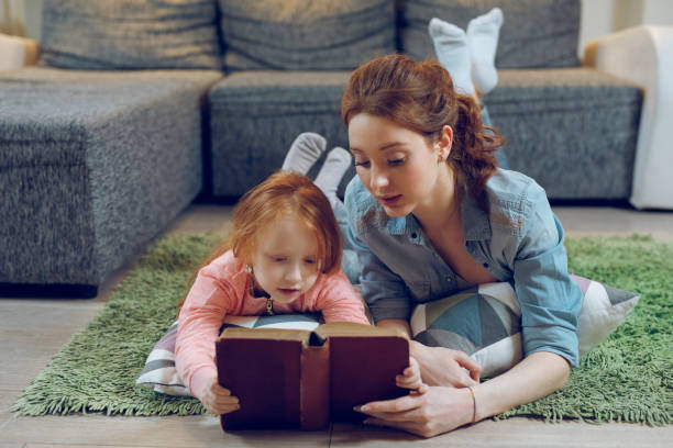 istock Mother reading a book to her daughter on carpet 948445132