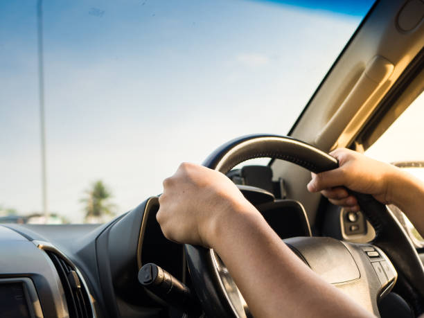 istock Man's hands holding steering wheel and road background. Driving concept 948445218