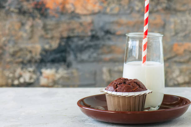 Homemade chocolate biscuit muffins next to bottle of milk on isolated background. Three homemade chocolate and cookie cupcakes next to a bottle of milk on white background