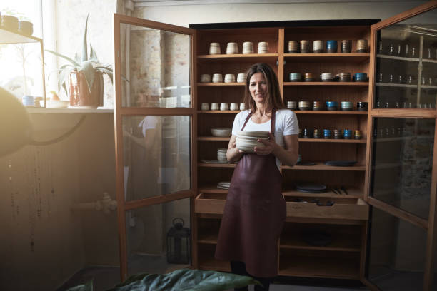 istock Smiling artisan standing with ceramic plates in her pottery studio 948455030