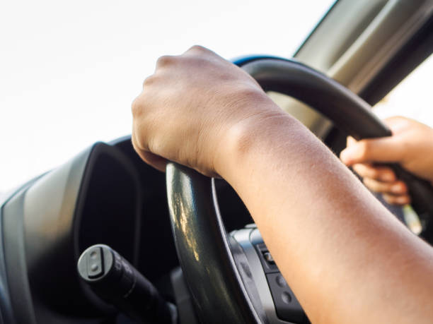 istock Man's hands holding steering wheel and road background. Driving concept 948459600