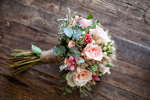 wedding bouquet of white and pink roses and peonies in the hands of the bride on the background of a white dress