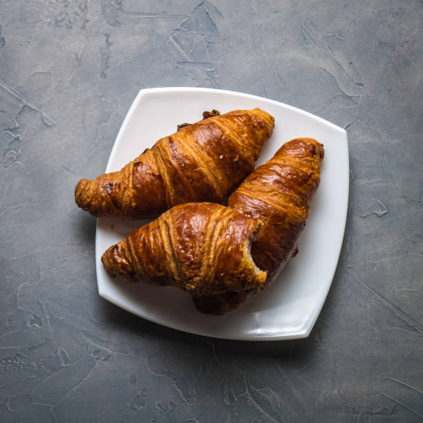 istock Three croissants and one bitten in a white saucer on a gray concrete background. 948472850