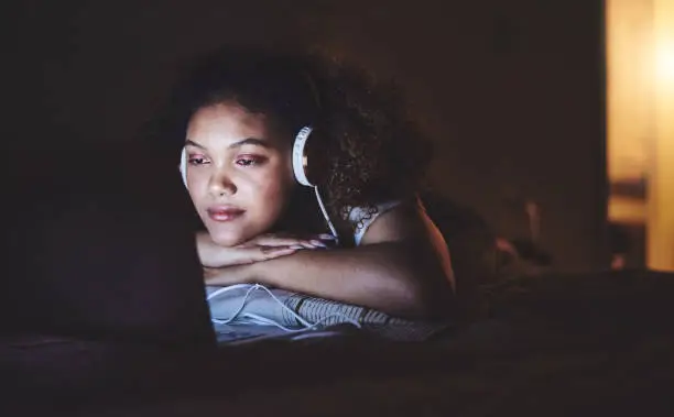 Shot of a young woman wearing headphones while using a laptop at home