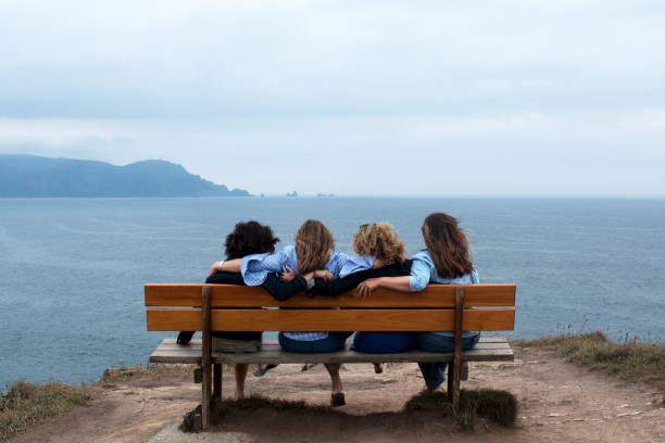istock Four 50-YEAR-OLD girlfriends hugging and staring at the horizon on a bench 948482700