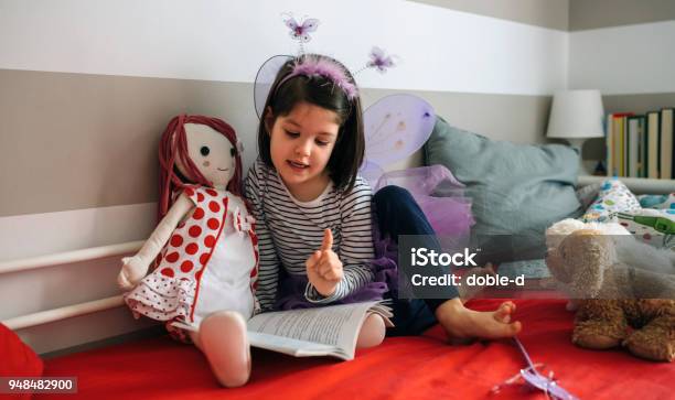 Ragazza Travestita Leggendo Un Libro Alla Sua Bambola - Fotografie stock e altre immagini di Bambino