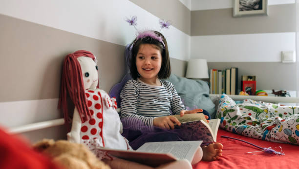 istock Girl disguised as a butterfly reading with her doll 948483040
