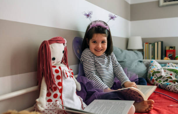 istock Girl disguised as a butterfly reading with her doll 948485208