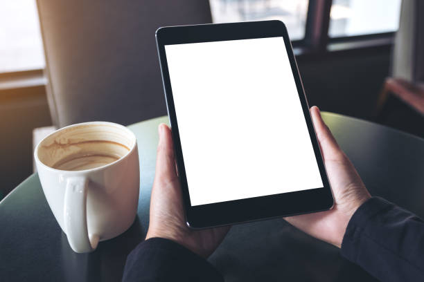 istock Mockup image of hands holding black tablet pc with blank white screen and coffee cup on table in cafe 948487640