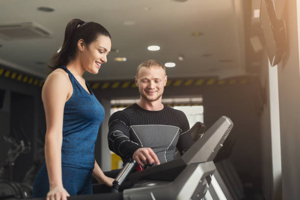 istock Fitness coach helps woman on elliptical trainer 948492640
