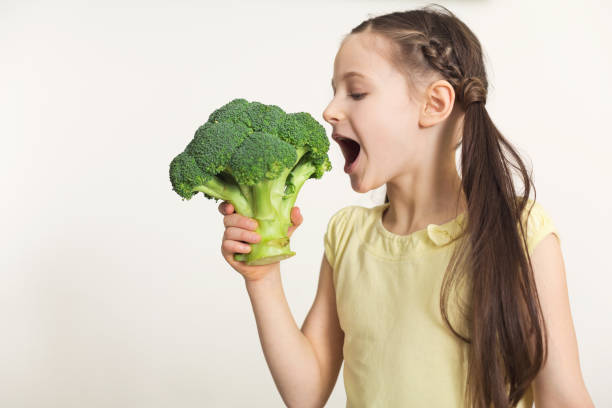istock Pretty cute little girl biting broccoli over white background 948495592
